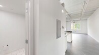 Located at 4151 Main St in Philadelphia's vibrant Manayunk neighborhood, this single-floor unit blends industrial character with modern finishes throughout. The open main living area makes a strong first impression with its soaring exposed steel truss ceiling, corrugated metal panels, and polished concrete floors — a nod to the building's industrial heritage. A ceiling fan with a brass-toned fixture adds a contemporary touch while keeping the space comfortable.

The galley-style kitchen is well-appointed, featuring white shaker cabinetry, granite countertops, a dark subway tile backsplash, and stainless steel appliances including a range, microwave, refrigerator, and dishwasher. Industrial pendant lighting hangs from the elevated ceiling, reinforcing the loft aesthetic. A peninsula with a built-in sink and additional counter space adds both functionality and a natural division between the kitchen and living area.

The bathroom is clean and modern, finished with large-format white tile flooring, a white vanity, and a stacked washer and dryer unit — providing the convenience of in-unit laundry. Crisp white walls throughout the space enhance brightness and create a neutral canvas. A hallway connects the key areas of the unit, contributing to an efficient and cohesive layout ideal for live-work or residential use.