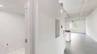 Located at 4151 Main St in Philadelphia's vibrant Manayunk neighborhood, this single-floor unit blends industrial character with modern finishes throughout. The open main living area makes a strong first impression with its soaring exposed steel truss ceiling, corrugated metal panels, and polished concrete floors — a nod to the building's industrial heritage. A ceiling fan with a brass-toned fixture adds a contemporary touch while keeping the space comfortable.

The galley-style kitchen is well-appointed, featuring white shaker cabinetry, granite countertops, a dark subway tile backsplash, and stainless steel appliances including a range, microwave, refrigerator, and dishwasher. Industrial pendant lighting hangs from the elevated ceiling, reinforcing the loft aesthetic. A peninsula with a built-in sink and additional counter space adds both functionality and a natural division between the kitchen and living area.

The bathroom is clean and modern, finished with large-format white tile flooring, a white vanity, and a stacked washer and dryer unit — providing the convenience of in-unit laundry. Crisp white walls throughout the space enhance brightness and create a neutral canvas. A hallway connects the key areas of the unit, contributing to an efficient and cohesive layout ideal for live-work or residential use.