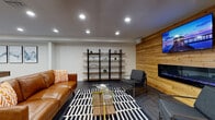 Rushwood Apartments offers a thoughtfully designed amenity level that caters to both relaxation and an active lifestyle. The welcoming lobby entrance features the community's bold branded signage, flanked by a pair of contemporary gray accent chairs and a cowhide area rug, setting an inviting first impression.

The centerpiece of the amenity space is a stylish lounge area anchored by a striking natural wood shiplap accent wall, which houses a sleek linear electric fireplace and a large wall-mounted television. A rich cognac leather sofa, modern gray armchairs, a glass-and-brass coffee table, and a bold black-and-white striped area rug come together to create a comfortable and sophisticated gathering space. An open industrial-style shelving unit adds functional display storage along the adjacent wall.

The fitness center is well-appointed with cardio equipment including treadmills, an elliptical, and a stationary bike, all reflected in floor-to-ceiling mirrors that amplify the space. A dedicated yoga and stretching studio features light hardwood-style flooring, full-wall mirrors, yoga mats, and medicine balls, offering a serene environment for mindful movement.

Connecting these spaces is an open corridor with dark hardwood-style flooring, leading to a game room complete with a billiards table and curated wall art, rounding out this comprehensive amenity offering.