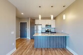 Located at 9763 Caspian Ct in Papillion, Nebraska, this one-bedroom, one-bathroom unit offers a thoughtfully designed layout that maximizes its efficient footprint. The open-concept kitchen and living area serves as the heart of the space, finished with light hardwood-style flooring that extends throughout the main area. The kitchen is well-appointed with granite countertops, a double undermount sink, stainless steel appliances including a refrigerator, electric range, and microwave, and a mix of white upper cabinetry and warm wood-toned lower cabinetry. A peninsula with pendant lighting above provides additional workspace and a natural divide between the kitchen and living area. The living room benefits from recessed lighting and a sliding glass door that opens to a private balcony, inviting natural light and outdoor views into the space. The bedroom features neutral carpet, soft wall tones, and a dedicated closet, offering a quiet and comfortable retreat. The bathroom includes a full tub and shower combination, a granite-topped vanity with wood cabinetry, and wood-style flooring, maintaining the consistent, contemporary aesthetic found throughout the unit. Overall, the space presents a clean, modern design with quality finishes throughout.