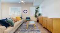 This single-floor unit in Phoenix, AZ offers a thoughtfully designed layout accommodating five bedrooms and two full bathrooms. Light wood-look flooring runs consistently throughout, creating a cohesive, modern aesthetic across all rooms.

The open-concept kitchen and living area serves as the heart of the unit. The kitchen features stainless steel appliances, white upper cabinetry, wood-toned lower cabinets, and a large island with a white countertop and bar seating beneath pendant lighting. The adjacent living room benefits from multiple windows providing ample natural light, and includes a ceiling fan overhead.

Each bedroom maintains a clean, neutral palette with white walls, wood-look flooring, and windows that bring in outdoor views. Bedrooms are equipped with sliding or hinged closet doors, offering practical storage. The primary bedroom provides a comfortable, well-proportioned space.

Both bathrooms follow a consistent design with wood-toned vanity cabinetry, white countertops, and a full shower-tub combination. The hallways connecting the rooms include a built-in shelf, adding functional detail. Overall, the unit presents a contemporary, streamlined ambiance well-suited to shared living.