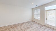 This generously sized one-bedroom, one-bathroom unit offers an expansive single-floor layout with contemporary finishes throughout. The kitchen is appointed with white shaker-style cabinetry, granite-style countertops, a subway tile backsplash, black stainless steel appliances including a refrigerator, electric range, microwave, and dishwasher, and light wood-look luxury vinyl plank flooring that extends into the adjoining living area. The open connection between the kitchen and living room creates a fluid, functional space suited for everyday living.

The bedroom features carpeted flooring, a ceiling fan, and natural light from a window with blinds, with direct access to a spacious walk-in closet outfitted with wire shelving along multiple walls. The bathroom includes a granite-top vanity, a framed mirror, wood-look flooring, and accessibility-friendly grab bars. A dedicated laundry room houses a full-size, side-by-side GE washer and dryer with overhead wire shelving. A covered patio provides outdoor access with views of the surrounding landscaped community.