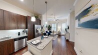 This thoughtfully designed single-floor residence offers a seamless blend of style and functionality. The open-concept layout connects the kitchen and living area, creating a welcoming, airy atmosphere enhanced by crown molding, rich hardwood-style flooring, and a ceiling fan with ample natural light filtering through large windows.

The kitchen is a standout feature, showcasing tall dark espresso cabinetry, granite countertops, a subway tile backsplash, stainless steel appliances — including a French door refrigerator with ice and water dispenser, dishwasher, and range — as well as a central island with seating, illuminated by stylish pendant lighting. The living area flows naturally from the kitchen, providing a comfortable and cohesive gathering space.

The bedroom is generously proportioned with plush carpeting and a large window that brings in natural greenery views. It is complemented by a walk-in closet outfitted with built-in shelving and hanging rods. A dedicated built-in desk nook with granite countertop and open shelving provides a practical workspace within the residence.

The bathroom continues the consistent design aesthetic with dark wood cabinetry, a granite vanity, hardwood-style flooring, and bright vanity lighting. Throughout, the space maintains a cohesive, modern-transitional character with high-quality finishes at every turn.
