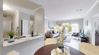 This single-floor, 2-bedroom, 2-bathroom residence offers a thoughtfully designed open-concept layout that seamlessly connects the main living areas. The kitchen is equipped with stainless steel appliances, including a gas range and microwave, and features a two-tone cabinet scheme with dark lower cabinets and white upper cabinets, complemented by white countertops and wood-style flooring. A breakfast bar connects the kitchen to the dining area, which showcases crown molding, track lighting, and a built-in desk nook framed by an elegant arched entry. The living room extends toward a sliding glass door, filling the space with natural light and providing access to an outdoor area. Both bedrooms are carpeted and well-sized, offering ceiling fans and ample natural light. The two full bathrooms each feature dark vanity cabinetry with white countertops, a tub-shower combination, and wood-style flooring. A dedicated in-unit laundry area accommodates a full-size washer and dryer. Throughout the residence, a neutral gray-and-white color palette, crown molding accents, and consistent wood-style flooring create a cohesive and modern aesthetic.
