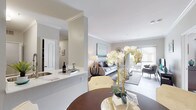 This single-floor, 2-bedroom, 2-bathroom residence offers a thoughtfully designed open-concept layout that seamlessly connects the main living areas. The kitchen is equipped with stainless steel appliances, including a gas range and microwave, and features a two-tone cabinet scheme with dark lower cabinets and white upper cabinets, complemented by white countertops and wood-style flooring. A breakfast bar connects the kitchen to the dining area, which showcases crown molding, track lighting, and a built-in desk nook framed by an elegant arched entry. The living room extends toward a sliding glass door, filling the space with natural light and providing access to an outdoor area. Both bedrooms are carpeted and well-sized, offering ceiling fans and ample natural light. The two full bathrooms each feature dark vanity cabinetry with white countertops, a tub-shower combination, and wood-style flooring. A dedicated in-unit laundry area accommodates a full-size washer and dryer. Throughout the residence, a neutral gray-and-white color palette, crown molding accents, and consistent wood-style flooring create a cohesive and modern aesthetic.