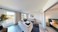 Located in the vibrant University District of Seattle, this contemporary single-floor residence at 4906 25th Ave NE offers a thoughtfully designed living experience. The open living area is bathed in natural light, courtesy of large floor-to-ceiling windows and a glass balcony door that frames treetop views of the surrounding neighborhood. Light hardwood-style flooring flows throughout, complementing the clean white walls and creating a bright, airy ambiance. A wall-mounted mini-split system ensures year-round climate comfort. The galley-style kitchen is efficiently laid out, featuring dark wood cabinetry, white countertops, a classic subway tile backsplash, and a full suite of stainless steel appliances, including a refrigerator, range, and microwave. The bedroom is a calm retreat, finished with soft neutral tones and featuring a frosted-glass sliding door that opens to a well-organized walk-in closet with built-in shelving and hanging space. The bathroom is clean and modern, offering warm wood-toned cabinetry, a white countertop vanity, and tile flooring. Throughout the residence, recessed lighting and a minimalist design aesthetic create a cohesive, contemporary feel that suits both everyday living and stylish entertaining.