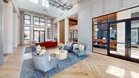 This 6,420-square-foot single-floor amenity clubhouse, branded "Monarch," offers a comprehensive suite of spaces designed for both relaxation and productivity. The entry features floor-to-ceiling glass doors with black metal frames, opening onto herringbone-pattern hardwood flooring that flows into a bright, open reception corridor with hexagonal tile and soaring high ceilings.

The main lounge is a standout space, showcasing coffered wood-accented ceilings, elegant chandelier lighting, herringbone hardwood floors, and vertical wood slat partitions that divide functional zones without obstructing natural light. A large-screen entertainment wall, billiards table, and plush seating areas with warm amber and neutral tones create an inviting social atmosphere.

A dedicated conference room features a substantial stone-topped table, leather seating, wall-mounted display, and tall ceilings illuminated by a modern pendant fixture. Private co-working nooks offer built-in stone desks, designer wallcoverings, and task lighting for focused work.

The fitness center is housed in a dramatic space with vaulted wood-plank ceilings, expansive multi-pane windows, and abundant natural light. It is fully equipped with strength machines, cardio equipment, a functional training rig, and turf flooring. Teal shiplap walls with stone accents add architectural character to the fitness entry area.