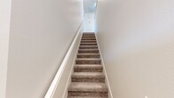 This two-floor residence offers a thoughtfully organized layout spread across four bedrooms, one bathroom, and a combined kitchen and living area. The entry level hosts the main living space, where an open-plan kitchen and living room create a bright, welcoming hub for daily life. The kitchen is outfitted with white shaker cabinetry, light quartz countertops, stainless steel appliances including a refrigerator, range, microwave, and dishwasher, and a peninsula with bar seating. Light hardwood-style flooring runs throughout, complementing the clean, neutral palette. The adjacent living and dining areas provide ample space for relaxing and entertaining, bathed in natural light from multiple windows. A carpeted staircase with crisp white walls connects the floors, leading to the upper level where the four bedrooms are located. Each bedroom features light-toned flooring, large windows bringing in natural light, and generous proportions — the primary bedroom offering notably spacious accommodations. The shared full bathroom is finished in white cabinetry with a combined tub and shower enclosure and wood-look flooring. A dedicated closet provides additional storage. The overall aesthetic is clean, modern, and move-in ready.