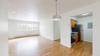 Located at 587 Broadway in Watervliet, NY, this two-bedroom, one-bathroom residence offers a well-organized single-floor layout with a clean, bright aesthetic throughout. Warm hardwood-style flooring runs continuously through every room, creating a cohesive and inviting atmosphere.

The open living area is bathed in natural light from a large multi-pane window, complemented by recessed lighting and a stylish pendant fixture. Baseboard heating runs along the perimeter, ensuring year-round comfort. The space flows seamlessly into the galley-style kitchen, which is equipped with warm wood cabinetry, granite countertops, a subway tile backsplash, and stainless steel appliances including a range, dishwasher, and refrigerator.

The primary bedroom is generously sized, featuring a wide bank of louvered sliding closet doors that provide abundant storage. The second bedroom includes its own window with outdoor views and baseboard heating. Three closets are distributed throughout the unit, offering exceptional storage capacity.

The bathroom is neatly appointed with a white vanity featuring shaker-style cabinetry, a mirror, and a separate shower/tub alcove with crisp white finishes. A connecting hallway ties all rooms together efficiently. Recessed lighting and white walls throughout lend the entire residence a fresh, move-in-ready feel.