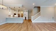 This two-story residence offers a generous 1650 square feet of living space, thoughtfully distributed across two floors. The ground floor spans 730 square feet, while the upper level provides an additional 920 square feet. The home boasts three bedrooms, including a spacious primary suite measuring 230 square feet, and an impressive seven bathrooms, ensuring ample privacy and convenience for occupants and guests alike.

The interior is characterized by its bright and airy atmosphere, thanks to large windows that flood the rooms with natural light. The image showcases a living area with pristine hardwood flooring, adding warmth and elegance to the space. High ceilings with a modern ceiling fan contribute to the sense of openness.

The open-concept design is evident, with a seamless flow between the living room and kitchen area. A pendant light fixture adds a touch of sophistication to the space. The neutral color palette, featuring soft beige walls, creates a versatile backdrop for various decor styles.

Additional features include three closets for storage, a staircase connecting the two floors, and a hallway for easy navigation. The combination of kitchen and living room in one area suggests a contemporary lifestyle-focused layout, perfect for entertaining or family gatherings.