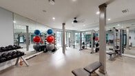 Located at 390 Stovall St SE in Atlanta, Georgia, this fitness center offers a comprehensive and thoughtfully organized workout facility. The space is finished with durable speckled flooring throughout, recessed lighting, and a ceiling fan that ensures proper air circulation during workouts. Structural columns are integrated into the open floor plan, adding an architectural element while maintaining a spacious feel.

Floor-to-ceiling mirrors line the walls, visually expanding the space and allowing users to monitor their form during exercise. Large windows along one side of the room invite natural light and provide views of the surrounding greenery, creating an energizing atmosphere.

The facility is well-stocked with a diverse range of equipment. A multi-station cable and weight machine anchors the strength training area, complemented by a dedicated weight bench and barbell setup. A tiered rack of dumbbells and a collection of kettlebells provide ample free weight options. Stability and medicine balls of various sizes are neatly stored on a dedicated rack. Selectorized resistance machines line the teal-accented rear wall, which adds a vibrant pop of color to the interior.

Additional amenities include a dual water fountain station for convenient hydration and a glass-paned entry door. The overall ambiance is clean, functional, and motivating, making it a well-rounded fitness resource.