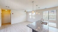 Located at 455 South Recker Road in Gilbert, Arizona, this well-appointed one-bedroom, one-bathroom residence offers a thoughtfully designed layout with modern finishes throughout. The open-concept kitchen and living area serves as the heart of the home, showcasing a large granite-topped island with a stainless steel sink and stylish pendant lighting overhead. The kitchen is equipped with dark espresso cabinetry extending to the ceiling, stainless steel appliances including a refrigerator, range, and microwave, and additional track lighting that brightens the workspace. Light wood-look flooring flows seamlessly through the kitchen and living area, complemented by a ceiling fan and multiple windows that fill the space with natural light. The spacious bedroom features plush carpeting and ample wall space, while the walk-in closet provides generous storage with multiple hanging rods and shelving. The bathroom is finished with a sleek dual-sink vanity with dark cabinetry, a large frameless sliding glass shower enclosure, and tile flooring. A dedicated laundry room houses a full-size side-by-side washer and dryer with built-in shelving for added convenience. Carpeted stairs are also present, indicating a multi-level layout within the unit.
