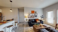 Located at 1001 Columbus Ave in Marysville, Ohio, this single-floor unit offers a thoughtfully designed layout that balances comfort and functionality. The open-concept kitchen is equipped with stainless steel appliances, including a full-size refrigerator, electric range, and over-the-range microwave. White cabinetry provides ample storage, while a peninsula with a double-basin sink and pendant lighting serves as a natural divider between the kitchen and living areas. Light wood-style flooring runs throughout the kitchen, transitioning to plush carpet in the living and sleeping areas. The living room is bright and welcoming, featuring a glass door that opens to an outdoor balcony, allowing for generous natural light. A bar-height counter with stools offers an additional casual dining option adjacent to the kitchen. The bedroom is generously proportioned, featuring tall ceilings, multiple large windows with views of the surrounding area, and warm neutral walls. The full bathroom includes a single-sink vanity with ample counter space, wood-style flooring, and direct access to a dedicated walk-in closet with built-in shelving. Throughout the space, a cohesive neutral color palette and clean architectural lines create a modern, move-in-ready environment.