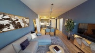 This single-floor residence showcases a thoughtfully designed open-concept layout that seamlessly connects the living, dining, and kitchen areas. Rich hardwood-style flooring runs throughout the main living spaces, complemented by bold slate-blue accent walls that lend the home a modern, sophisticated character.

The kitchen is fully equipped with stainless steel appliances, including a gas range, microwave, and refrigerator. Dark gray shaker-style cabinetry pairs elegantly with granite countertops and a classic white subway tile backsplash, while under-cabinet lighting adds a refined finishing touch. A stainless steel sink and dishwasher complete this functional and stylish culinary space.

The open living and dining area is anchored by warm pendant lighting and a globe chandelier above the dining table, creating an inviting atmosphere. The living room offers ample space for relaxed seating, with natural light filtering in through slatted window treatments.

The primary bedroom is a serene retreat, featuring plush carpet flooring, a large window with outdoor views, and a striking spherical chandelier. A vibrant yellow accent chair adds a pop of color against the cool-toned walls. The second bedroom is equally comfortable, with soft carpet and a copper-toned chandelier.

Both bathrooms are finished with gray shaker vanities, white countertops, and neutral tile flooring, with one offering a full soaking tub and shower combination.