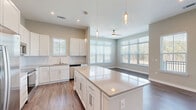 Located at 4600 Bakers Blessing Ln in Summerville, SC, this well-appointed single-story home offers 2 bedrooms, 3 bathrooms, and a thoughtfully designed open floor plan. The kitchen and living area flow seamlessly together, anchored by a large center island with a light quartz countertop, white shaker-style cabinetry extending to the ceiling, and a full suite of stainless steel appliances including a refrigerator, electric range, built-in microwave, and dishwasher. Elegant pendant lighting and a ceiling fan complement the bright, airy atmosphere created by abundant natural light pouring through multiple large windows with blinds. Hardwood-style flooring runs throughout the main living areas, while plush carpet adds warmth to the bedrooms. The spacious primary bedroom includes a generous walk-in closet outfitted with wire shelving. A second well-sized bedroom also enjoys natural light through large windows. The hallways are clean and open with neutral gray tones throughout, recessed lighting, and crisp white trim. With three full bathrooms and a dedicated closet, this home balances functional storage with comfortable living in a modern, move-in-ready package.