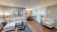 This single-floor residence offers a thoughtfully designed layout that balances comfort and functionality throughout. The open-concept living and dining area serves as the heart of the home, featuring warm hardwood-style flooring, recessed lighting, and large windows dressed with vertical blinds that invite generous natural light and views of surrounding greenery. The living space provides ample room for relaxed seating arrangements, while the adjacent dining area is illuminated by an elegant chandelier, creating an inviting atmosphere for everyday meals or entertaining.

The kitchen is equipped with rich oak cabinetry, granite-style countertops, a double-basin sink, and a dishwasher, all complemented by recessed ceiling lights and the same hardwood-style flooring that flows through the common areas.

The bedroom is a serene retreat, carpeted for comfort and filled with natural light through large windows. It features a sliding-door closet with built-in shelving and dresser space, providing ample storage. The bathroom showcases a wide vanity with granite-style countertops, warm wood cabinetry, a large mirror, and an additional storage cabinet, offering both style and practicality.

Neutral gray wall tones throughout the residence create a cohesive, modern aesthetic, contributing to an overall ambiance that is calm, bright, and welcoming.