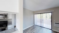 Located at 5925 El Cajon Blvd in San Diego, Unit #309 is a single-floor residence that combines clean, modern design with a comfortable and functional layout. The living area is finished with smooth, wood-look luxury vinyl plank flooring in a cool grey tone, providing a contemporary foundation throughout the space. Neutral grey walls and crisp white trim create a bright, cohesive atmosphere that feels open and welcoming. A textured ceiling adds a classic touch overhead. A large sliding glass door fitted with vertical blinds fills the living area with abundant natural light and opens to a private balcony that overlooks a lush, tree-lined setting — offering a pleasant sense of greenery and privacy. A partial dividing wall separates the living area from the kitchen, which features granite-look countertops visible from the main living space, contributing to the unit's updated aesthetic. A panel door is visible leading to additional areas of the unit. The overall ambiance is clean, airy, and move-in ready, making it a well-appointed residence in the heart of San Diego.