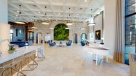 This impressive single-floor amenity space is defined by its sophisticated architectural design and upscale finishes throughout. The grand lobby serves as the centerpiece, featuring soaring coffered ceilings, stacked stone accent walls with arched openings, and a striking living moss wall bursting with lush greenery and vibrant color. A white grand piano and an arrangement of modern pendant lights add elegance to the expansive main hall, which is finished with large-format travertine-style tile flooring.

Multiple seating areas are thoughtfully distributed throughout the space, including a curated lounge with plush armchairs and textured barrel chairs, a formal sitting room adorned with bold artwork and tall windows flooding the area with natural light, and a cozy nook featuring a built-in bench against a herringbone-tiled wall.

The social kitchen area is equipped with a substantial island topped with dramatic veined stone countertops, a built-in gas range, and bar seating — complemented by a pool table and lounge furniture nearby for entertainment. A dining area with floor-to-ceiling steel-framed windows overlooks a resort-style outdoor pool surrounded by palm trees, seamlessly blending indoor and outdoor living. A dedicated workspace corridor with task seating, curated art, and ample natural light rounds out this well-appointed communal facility.