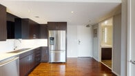 Located at 1914 Commerce St in the heart of downtown Dallas, this single-floor unit presents a clean, contemporary design highlighted by rich hardwood flooring that extends throughout the open living areas. The kitchen is a standout feature, outfitted with a full suite of stainless steel appliances including a French door refrigerator, electric range, built-in microwave, and dishwasher. Dark espresso-toned cabinetry reaches toward the ceiling, providing generous storage, while a white tile backsplash and light countertops offer a sharp visual contrast. The open layout connects the kitchen seamlessly to the living area, creating a cohesive and functional space. Large windows frame striking views of the downtown Dallas skyline, flooding the interior with natural light. The bedroom also benefits from dual windows with city views and includes a ceiling fan for added comfort. The bathroom is finished in a neutral palette, featuring a combined tub and shower with a rainfall-style showerhead, a vanity with a lighted mirror, and tile flooring. Recessed lighting and a neutral gray wall color throughout contribute to the unit's modern, urban aesthetic.