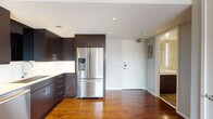 Located at 1914 Commerce St in the heart of downtown Dallas, this single-floor unit presents a clean, contemporary design highlighted by rich hardwood flooring that extends throughout the open living areas. The kitchen is a standout feature, outfitted with a full suite of stainless steel appliances including a French door refrigerator, electric range, built-in microwave, and dishwasher. Dark espresso-toned cabinetry reaches toward the ceiling, providing generous storage, while a white tile backsplash and light countertops offer a sharp visual contrast. The open layout connects the kitchen seamlessly to the living area, creating a cohesive and functional space. Large windows frame striking views of the downtown Dallas skyline, flooding the interior with natural light. The bedroom also benefits from dual windows with city views and includes a ceiling fan for added comfort. The bathroom is finished in a neutral palette, featuring a combined tub and shower with a rainfall-style showerhead, a vanity with a lighted mirror, and tile flooring. Recessed lighting and a neutral gray wall color throughout contribute to the unit's modern, urban aesthetic.