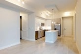 This single-floor residence showcases a clean, modern aesthetic defined by an open-concept design that connects the kitchen and living area in one cohesive, light-filled space. The kitchen is a standout feature, equipped with stainless steel appliances including a range, microwave, dishwasher, and refrigerator. A central island with a crisp white countertop provides additional workspace and serves as a natural gathering point. Sleek two-tone cabinetry — combining white upper cabinets with warm wood-toned lower units — adds visual depth, while a white tile backsplash and track lighting overhead maintain the bright, contemporary feel. Pendant lights hang elegantly above the island, contributing both function and style. The open living area extends naturally from the kitchen, featuring light-toned flooring throughout that enhances the sense of space and airiness. A ceiling fan is installed in the living area, adding comfort alongside practical ventilation. A sliding glass door allows natural light to filter in and provides access to the outdoors. Louvered closet doors and a paneled entry door add thoughtful architectural detail, while the overall neutral color palette creates a versatile, welcoming ambiance throughout the home.