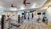 Located at 1731 Tupelo Hill Ln in Raleigh, NC, this single-floor fitness facility is thoughtfully designed to support a comprehensive range of workout disciplines. The space is divided into distinct functional zones, each finished to a high standard and unified by warm wood-look flooring, crisp white walls, and recessed lighting complemented by ceiling fans throughout.

The main strength and conditioning area is generously proportioned, housing a multi-functional power rack with TRX suspension systems, a heavy bag, selectorized weight machines, free-weight benches, and a variety of resistance equipment. Wall-mounted flat-screen televisions and artwork add a polished, motivating atmosphere. Large windows with plantation-style blinds invite natural light while maintaining privacy.

A dedicated cardio zone features multiple treadmills, elliptical trainers, and step machines, each positioned to allow comfortable spacing and accompanied by mounted televisions for entertainment during workouts.

A separate studio room showcases a striking herringbone-patterned hardwood floor beneath a tray ceiling, creating an elegant and open environment ideal for yoga, cycling, barre, and functional training. This room is equipped with spin bikes, stability balls, resistance accessories, a wall-mounted ballet barre, and a mirrored wall. Decorative multi-panel artwork and expansive windows enhance the bright, airy ambiance. A glass-paneled interior window connects this studio to adjacent areas, reinforcing the open and interconnected layout of the facility.