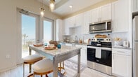 Located at 1216 N Atlantic Ave in Daytona Beach, FL, this well-appointed one-bedroom, one-bathroom unit offers a thoughtfully designed layout across a single floor. The open-concept kitchen is a standout feature, showcasing crisp white shaker cabinetry, a white subway tile backsplash, granite countertops, and a full suite of stainless steel appliances including a range, over-the-range microwave, and refrigerator. Pendant lighting illuminates a central island with bar seating, creating an inviting space for dining and entertaining. Large windows flood the kitchen and living areas with abundant natural light, with views that hint at the nearby Atlantic Ocean. The living room features light wood-style flooring, soaring ceilings, and a neutral color palette that enhances the sense of openness. The bedroom is a serene retreat with a window offering ocean views, tall ceilings, and soft carpet underfoot. It connects directly to the bathroom, which features a spacious walk-in shower clad in marble-style tile, a granite-topped vanity, and light wood-tone flooring. A dedicated walk-in closet with built-in wire shelving provides ample storage. Light, airy, and coastal in feel, this unit is ideally situated steps from the beach.