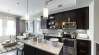 This well-appointed 2-bedroom, 2-bathroom residence offers a thoughtfully designed single-floor layout that balances style and functionality. The open-concept kitchen serves as the heart of the home, showcasing rich dark cabinetry that contrasts beautifully with light granite countertops. Stainless steel appliances, including a range and built-in microwave, provide a sleek, modern aesthetic. A subway tile backsplash adds a classic yet contemporary touch, while an expansive kitchen island with seating creates an ideal space for casual dining and entertaining. Pendant lighting fixtures hang above the island, complementing the track lighting overhead to create a warm, layered ambiance. The kitchen flows seamlessly into the living area, which benefits from natural light and offers space for comfortable furnishings. Open shelving within the cabinetry provides both storage and an opportunity for thoughtful décor display. The overall design palette—neutral tones, dark wood accents, and polished surfaces—creates a cohesive and sophisticated atmosphere throughout. The two bedrooms offer private retreats, while the two full bathrooms add convenience for residents and guests alike.
