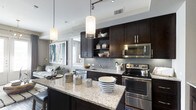 This well-appointed 2-bedroom, 2-bathroom residence offers a thoughtfully designed single-floor layout that balances style and functionality. The open-concept kitchen serves as the heart of the home, showcasing rich dark cabinetry that contrasts beautifully with light granite countertops. Stainless steel appliances, including a range and built-in microwave, provide a sleek, modern aesthetic. A subway tile backsplash adds a classic yet contemporary touch, while an expansive kitchen island with seating creates an ideal space for casual dining and entertaining. Pendant lighting fixtures hang above the island, complementing the track lighting overhead to create a warm, layered ambiance. The kitchen flows seamlessly into the living area, which benefits from natural light and offers space for comfortable furnishings. Open shelving within the cabinetry provides both storage and an opportunity for thoughtful décor display. The overall design palette—neutral tones, dark wood accents, and polished surfaces—creates a cohesive and sophisticated atmosphere throughout. The two bedrooms offer private retreats, while the two full bathrooms add convenience for residents and guests alike.