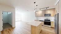Located at 2311 Dulles Station Blvd in Herndon, Virginia, this single-floor residence offers a clean, modern aesthetic defined by light wood flooring, crisp white walls, and an open, airy layout. The centerpiece of the home is a well-appointed kitchen that seamlessly connects to the living area, creating an inviting open-concept space. The kitchen is outfitted with light wood cabinetry, a classic subway tile backsplash, white quartz countertops, and a full suite of stainless steel appliances, including a range, microwave, dishwasher, and refrigerator. A central island with additional storage provides extra prep space and serves as a natural gathering point. Pendant lighting and a track light system illuminate the kitchen and living areas with both functional and ambient light. The living area benefits from natural light through large windows fitted with horizontal blinds. A dedicated bedroom features soft carpeting, transom windows that draw in additional natural light, and a bright, neutral palette that enhances the sense of space. Additional rooms continue the home's light and modern design, with consistent wood-tone flooring and clean white finishes. The overall ambiance is contemporary, bright, and welcoming, with thoughtful details that lend the space a polished, move-in-ready feel.