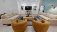 Located at 230 North 6th St in Richmond, Virginia, this community room offers a well-appointed, single-floor space designed for both relaxed socializing and functional gatherings. The layout is thoughtfully organized into distinct zones that flow seamlessly into one another.

The lounge area serves as the visual centerpiece, anchored by a neutral-toned sofa, plush mustard-yellow accent chairs, and a rustic wood coffee table set atop a patterned area rug. A teal-painted accent wall adds a pop of color against the otherwise crisp white walls, while pendant lighting and an arched floor lamp in brushed gold provide warm ambient illumination. A wall-mounted flat-screen TV and curated artwork complete the inviting atmosphere. A full-length arched mirror and lush indoor plants enhance the sense of openness and life throughout the space.

The kitchen is fully equipped with warm-toned wood cabinetry, dark granite countertops, stainless steel appliances including a large refrigerator, range, and built-in microwave, and a peninsula with bar seating for multiple guests — ideal for catering or community events.

A dedicated dining area with a round table and chairs provides additional seating, while light-toned flooring throughout ties the entire space together. Natural light filters in through windows, contributing to the room's bright and welcoming character.