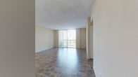 Located at 1600 NE 135th St in North Miami, Florida, this single-floor residence offers a functional and well-appointed layout designed for comfortable living. The open living area is finished with durable stone-look tile flooring and features a sliding glass door framed by vertical blinds, providing direct access to a private balcony and allowing natural light to fill the space. The galley-style kitchen is efficiently organized with warm wood cabinetry, granite-look countertops, a tile backsplash, and white appliances including a range, refrigerator, and dishwasher. Recessed lighting adds a clean, finished look to the kitchen ceiling. The bedrooms are carpeted for warmth and comfort, with one featuring a large double-door closet and a floor-to-ceiling window that brings in generous natural light and outdoor views. A second bedroom offers a cozy, quiet atmosphere with plush carpeting and neutral-toned walls. The unit includes two bathrooms: one with a soaking tub and granite-topped vanity, and another with a walk-in shower stall, both finished with stone-look tile flooring and chrome fixtures. Textured ceilings and warm beige walls throughout lend a consistent, neutral palette that complements a variety of interior styles.