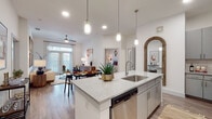 This single-story residence offers a thoughtfully designed open-concept layout that seamlessly connects the kitchen, dining, and living areas. The kitchen serves as a central hub, anchored by a large island with quartz countertops, an integrated sink, and seating for multiple guests. Gray shaker-style cabinetry, a subway tile backsplash, and a full suite of stainless steel appliances complete the space, while pendant lighting adds warmth overhead. A distinctive arched wood-framed mirror accent adds a rustic-modern touch near the kitchen entrance.

The living area flows naturally from the kitchen, featuring wood-style flooring, a ceiling fan, and large French doors that invite abundant natural light. Multiple bedrooms provide comfortable retreats, each with plush carpeting, generous windows with blinds, and ample wall space. The bathrooms are finished with light tile flooring, quartz-topped vanities, large mirrors, and walk-in closets with built-in shelving and hanging rods. A second full bathroom mirrors this clean, neutral aesthetic. Throughout the residence, white walls, recessed lighting, and consistent finishes create a cohesive, contemporary ambiance.