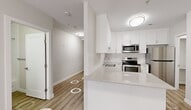This 2-bedroom, 2-bathroom unit at 10001 Bellamy Hill Rd NW offers a thoughtfully designed single-floor layout that makes excellent use of its space. Light wood-look flooring flows consistently throughout, complemented by crisp white walls and flush-mount lighting that maintain a clean, modern aesthetic.

The open kitchen is a standout feature, showcasing white shaker-style cabinetry, a white quartz countertop peninsula, subway tile backsplash, and a full suite of stainless steel appliances including a refrigerator, range, and over-the-range microwave. Adjacent to the kitchen, the living area benefits from natural light through a large window and includes an electric fireplace with baseboard heating.

Both bedrooms are bright and functional, each equipped with windows fitted with roller blinds and baseboard heating units. The primary bedroom offers a comfortable footprint with dedicated closet space. The two bathrooms are finished with quartz-topped vanities, white cabinetry, and clean tilework, with one featuring a full soaker tub and shower combination.

The hallways are well-lit and lined with mirrored sliding closet doors, adding a sense of depth. A dedicated laundry area houses a stacked washer and dryer unit alongside additional cabinetry for storage. Overall, the unit presents a modern, move-in-ready interior with consistent finishes throughout.