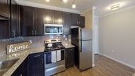 This single-floor residence offers a well-designed open-concept layout that seamlessly connects the living and kitchen areas. The kitchen is a standout feature, equipped with dark espresso cabinetry that extends to the ceiling, granite countertops, a tile backsplash, and a full suite of stainless steel appliances including a refrigerator, range, microwave, and dishwasher. A central island with matching granite provides additional prep space and serves as a natural dividing point between the kitchen and the expansive living area, which features warm wood-look flooring and crown molding throughout.

The bedrooms are finished with plush wall-to-wall carpeting and ceiling fans, offering a comfortable and functional retreat. Natural light filters in through windows fitted with blinds. A spacious walk-in closet equipped with wire shelving systems provides generous storage capacity.

The bathrooms are thoughtfully appointed with dark vanity cabinetry, granite countertops, framed mirrors, and bright vanity lighting. The full bathroom features a soaking tub with a tiled surround and an overhead shower. The overall color palette of neutral tones throughout creates a cohesive, clean aesthetic that is both modern and inviting.