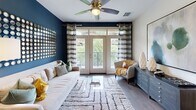 Located in Scottsdale, AZ, this well-appointed 2-bedroom, 2-bathroom residence offers a thoughtfully designed single-level layout that balances style and functionality. The open-concept kitchen and living area serves as the heart of the home, featuring dark espresso cabinetry with glass-front uppers, stainless steel appliances, a subway tile backsplash, and a large center island with a white quartz countertop and bar seating — ideal for both cooking and entertaining. Track and pendant lighting illuminate the space, while wood-style flooring adds warmth throughout. The living room is anchored by a bold navy accent wall, a ceiling fan, and French doors that open to an outdoor area with greenery views, filling the space with natural light. The primary bedroom is a comfortable retreat with plush carpet, a ceiling fan, generous natural light from large windows, and access to a walk-in closet. The en-suite bathroom features dark cabinetry, dual sinks with white quartz countertops, large-format tile flooring, and a glass-enclosed shower. The second bathroom mirrors this refined aesthetic with dual vanities and dark-framed mirrors. Both bedrooms offer ample closet space with built-in shelving systems, completing this polished Scottsdale residence.