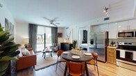 Located at 18301 S Dixie Hwy in Palmetto Bay, Florida, this single-floor residence offers a well-appointed, open-concept layout that seamlessly connects the kitchen, dining, and living areas. The kitchen is outfitted with stainless steel appliances, including a large French door refrigerator and a range with microwave, complemented by crisp white upper cabinetry, warm wood-toned lower cabinets, and a classic tile backsplash. A round dining table with cognac leather chairs sits adjacent to the kitchen, creating an inviting space for everyday meals. The living area features light wood-style flooring throughout, a ceiling fan, and floor-to-ceiling sliding glass doors that open to a private balcony, filling the space with natural light and outdoor views. The unit includes two distinctly designed bedrooms. The primary bedroom showcases a bold wood-paneled accent wall with an American flag artwork, dark charcoal walls, and a large window with roller shades. The second bedroom offers a cozy, eclectic aesthetic with antler-inspired wall décor, layered textiles, and a window with linen drapes. Both bedrooms continue the warm wood-style flooring found throughout the residence, maintaining a cohesive and contemporary feel across the entire unit.