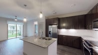 This single-floor, 1-bedroom, 1-bathroom residence offers a thoughtfully designed layout with modern finishes throughout. The kitchen serves as the centerpiece of the living area, showcasing rich dark cabinetry that extends to the ceiling for generous storage, granite countertops, and a full suite of stainless steel appliances including a French door refrigerator with ice maker, electric range, microwave, and dishwasher. A large kitchen island with a double-basin sink and pendant lighting overhead adds both functionality and style, while a white subway tile backsplash ties the space together. Wood-look flooring runs throughout the main living areas, lending warmth and continuity. The bedroom is a comfortable retreat featuring plush carpeting, a ceiling fan, and a window with natural light and outdoor views. The bathroom is well-appointed with dark wood double vanity cabinetry, granite countertops, a soaking tub, and tiled shower. A walk-in closet adjacent to the bathroom provides ample storage with wire shelving systems. Completing the unit is a dedicated in-unit laundry area with a full-size washer and dryer, offering added convenience. The overall ambiance is clean, modern, and move-in ready.