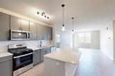 Located at 464 Glenwood Ave in Glen Ellyn, IL, this well-appointed 2-bedroom, 2-bathroom residence offers a thoughtfully designed single-floor layout with modern finishes throughout. The open-concept kitchen and living area serves as the heart of the home, featuring grey cabinetry, white quartz countertops, a subway tile backsplash, and a full suite of stainless steel appliances including a gas range, built-in microwave, dishwasher, and refrigerator. A large center island provides additional prep and dining space, while pendant lighting and a track light fixture add a contemporary touch. Light wood-tone flooring flows seamlessly into the spacious living room, which is brightened by multiple windows offering outdoor views of the surrounding greenery. The generously sized primary bedroom includes large windows that invite natural light, with direct access to a well-organized walk-in closet featuring built-in shelving and hanging rods. The bathrooms are clean and functional, with one offering a full soaking tub and shower combination. A dedicated in-unit laundry room houses a full-size washer and dryer alongside additional storage. The overall aesthetic is fresh, neutral, and move-in ready.