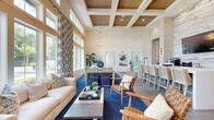 Located along Flagler Promenade Way in Maitland, FL, this thoughtfully designed single-floor space offers a generous layout encompassing a living room, dining room, and office. The interior is defined by soaring ceilings, expansive floor-to-ceiling windows, and an abundance of natural light that flows throughout. A coastal-inspired aesthetic ties the space together, with a neutral palette accented by blue tones, stone-clad accent walls, and a mix of tile and wood-look flooring.

The living room impresses with dramatic double-height windows dressed in bold patterned drapery, an elegant chandelier, and lush greenery that enhances the bright, airy atmosphere. Views of the surrounding palm-lined landscape further elevate the ambiance.

The dining area is anchored by a long white communal table with bar-height seating, set against a striking stacked-stone wall. A wood-beamed ceiling with recessed lighting and pendant fixtures adds warmth, while a pool table nearby offers a recreational focal point.

The office spaces are light-filled and functional, featuring clerestory windows that invite natural light while maintaining privacy. Lush outdoor views of tropical foliage create a serene work environment. Together, these rooms deliver a polished, welcoming, and highly functional space.