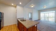 This single-floor residence is thoughtfully designed with a functional, open layout that connects the kitchen and living areas seamlessly. The kitchen is well-appointed with rich wood cabinetry, granite countertops, and a center island featuring a double stainless steel sink. Black appliances, including a refrigerator, electric range, and over-the-range microwave, provide a bold contrast to the warm wood tones and light hardwood flooring throughout the kitchen and entry areas.

The living area is generously sized, finished with plush carpeting, and benefits from natural light streaming through a large sliding glass door that opens to a private balcony, offering views of the surrounding area. An additional carpeted bedroom with a window provides further access to natural light and outdoor views.

The unit includes two bathrooms, each consistently finished with granite-topped wood vanities, large mirrors with bar lighting, and tile-style flooring. One bathroom features a full soaking tub and shower combination, while the other includes a shower. Both offer clean, neutral aesthetics that complement the overall design.

The bedrooms are carpeted and bright, with ample closet space including double-door closets. Throughout the unit, white walls and neutral tones create a clean, cohesive ambiance suited for comfortable everyday living.