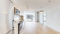Located in the heart of Montréal, this contemporary one-bedroom, one-bathroom unit at 1020 Rue De Bleury offers a well-designed layout with modern finishes throughout. Light hardwood flooring flows seamlessly across the open-concept living and kitchen area, creating a bright and cohesive aesthetic.

The kitchen is equipped with a full suite of stainless steel appliances, including a built-in microwave, electric range, dishwasher, and refrigerator. Sleek white cabinetry with a subway tile backsplash lines the walls, complemented by a pendant light fixture that anchors the space. Floor-to-ceiling windows in the living area flood the unit with natural light and offer sweeping views of the Montréal cityscape.

The bedroom features exposed concrete ceilings that add an industrial character, along with light hardwood floors and a tall vertical window framing urban views. Two closets provide ample storage. A dedicated hallway connects the main living areas to the bathroom, which includes a glass-enclosed walk-in shower with large-format grey tile and clean, modern fixtures.

A welcoming entry hallway completes the layout, offering a practical transition into the unit. The overall design balances minimalist aesthetics with functional living in a vibrant downtown Montréal location.