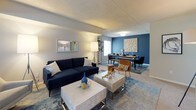 This single-floor residence offers a thoughtfully arranged layout with distinct living, dining, sleeping, and kitchen areas. The combined living and dining space is a standout feature, with the living area accommodating comfortable seating alongside a large window that brings in natural light and outdoor views. The dining zone is defined by a bold blue accent wall, adding a striking visual contrast to the otherwise neutral color palette used throughout the home.

The kitchen is well-appointed with light oak cabinetry, granite-toned countertops, and a full suite of white appliances including a range, dishwasher, and built-in microwave. Light wood-style flooring grounds the space with a warm, practical finish.

The primary bedroom is generously sized, featuring plush carpeting, a wide window overlooking greenery, and direct access to an en-suite bathroom equipped with a walk-in shower and mirrored medicine cabinet. A second bedroom provides flexible use as a sitting room or guest space, complete with a closet and natural light. A second full bathroom, finished in crisp white tones, serves the remaining areas of the home. Neutral walls and carpeting throughout create a cohesive, calm ambiance.