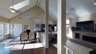 Located in Arlington, Texas, this single-story home showcases a striking open-concept design anchored by dramatic vaulted ceilings with exposed beams and a skylight that floods the interior with abundant natural light. Rich, dark hardwood flooring flows throughout the main living areas, creating a warm and cohesive aesthetic.

The living area is generously proportioned, offering ample space for comfortable seating arrangements, and transitions effortlessly into the dining area, which features a round dining table well-suited for gatherings. Structural columns define zones within the open floor plan while preserving the airy, expansive feel of the interior.

The kitchen is equipped with dark cabinetry, stainless steel appliances including a full-size refrigerator, and a functional layout that keeps it visually connected to the rest of the living space. Track lighting and recessed fixtures provide focused illumination throughout.

Large windows with plantation shutters line the walls, inviting natural light while offering privacy and light control. A ceiling fan enhances comfort in the open living zone. The overall ambiance is bright, spacious, and welcoming, combining practical design with notable architectural character that makes this Arlington home distinctly appealing.