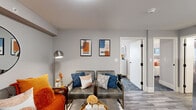 Located at 101 Cedar St in Providence, Rhode Island, this single-floor residence offers a thoughtfully designed layout with modern finishes throughout. The living area serves as the heart of the home, featuring light gray walls, wood-look flooring, and a cozy seating arrangement accented by vibrant orange and blue tones. A round wall mirror and contemporary abstract artwork add character, while a hallway connects the space to the rest of the unit. The kitchen is outfitted with crisp white shaker-style cabinetry, a white tile backsplash, and a full suite of stainless steel appliances, including a refrigerator with ice maker, electric range, over-the-range microwave, and dishwasher. Wood-look flooring continues seamlessly into this space. The unit includes two bedrooms, each with plush carpeting and natural light from sizable windows offering exterior views. One bedroom features a tufted gray headboard and a white dresser, while the other showcases a bold white lattice headboard with warm, neutral tones. The full bathroom is finished in a clean white palette with a vanity featuring shaker cabinetry, matte black fixtures, a tub-shower combination, and wood-look tile flooring. In-unit laundry is also visible, adding everyday convenience to this move-in-ready residence.