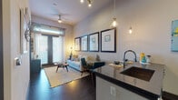 This thoughtfully designed single-floor residence offers a seamless blend of modern style and functional living. The open-concept layout connects the kitchen and living area, creating an inviting, airy atmosphere enhanced by rich dark hardwood flooring and soaring ceilings. The kitchen is outfitted with stainless steel appliances, crisp white cabinetry, a dark granite countertop, a tasteful tile backsplash, and a breakfast bar with pendant lighting — ideal for both meal preparation and casual dining. The living area is anchored by a ceiling fan, track lighting, and large windows with access to an outdoor area, allowing abundant natural light to fill the space. A gallery wall featuring a series of coordinating framed artwork adds a polished, curated touch. The bedroom is a serene retreat, featuring carpet flooring, generous windows dressed with blinds and sheer curtains, and ample natural light. The bathroom is finished with large-format floor and wall tiles, a glass-enclosed walk-in shower, a white vanity with dark countertop, and contemporary fixtures, delivering a clean and sophisticated aesthetic. Throughout the residence, the cohesive use of neutral tones, modern hardware, and carefully selected design details creates a welcoming and refined living environment.