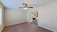 This two-story residence offers a straightforward, functional layout across two levels connected by a central staircase. The main living area features soft carpeting and a ceiling fan with integrated lighting, flowing openly into the kitchen. The kitchen is well-equipped with warm honey-toned wood cabinetry lining both walls, white appliances including an electric range, dishwasher, and refrigerator, a stainless steel sink, and durable hardwood-style flooring. A dedicated laundry area with washer and dryer hookups is conveniently located just off the kitchen, with a window that allows natural light into the space. The bedrooms are carpeted and comfortably sized, each featuring ceiling fans and windows fitted with horizontal blinds that provide both light control and privacy. The bathroom includes a vanity with wooden cabinetry, a toilet, and a clean white tub and shower combination with chrome fixtures. Additional storage is provided by a closet accessible from the hallway near the bathroom. Throughout the home, neutral warm-toned walls and clean white trim create a cohesive, understated aesthetic that offers a versatile canvas for personalization. The overall layout is practical and efficient, making good use of the available space across both floors.