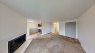 Located in University Place, WA, this one-bedroom, one-bathroom unit offers a practical and well-organized single-floor layout. The galley-style kitchen is a functional standout, featuring dark charcoal cabinetry with brushed nickel hardware, light speckled countertops, wood-look flooring, and white appliances including a refrigerator and electric range with oven. A ventilation hood and ample upper and lower cabinet storage complete the space.

The combined living room and dining area is carpeted and bathed in natural light through a large sliding glass door that opens to a private balcony with outdoor views. A fireplace adds a cozy focal point, and in-unit washer/dryer hookups provide added convenience. The space transitions smoothly from wood-look flooring near the entryway to plush carpeting throughout the main living areas.

The bedroom is a well-proportioned, carpeted retreat with a window overlooking greenery, a textured ceiling, baseboard heating, and a double sliding-door closet offering generous storage. The bathroom features a clean, all-white tub and shower combination with chrome fixtures. Throughout the unit, textured ceilings, bright white walls, and baseboard heating create a simple, consistent aesthetic.