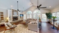 Located at 32 Olde Eastwood Village Blvd in Asheville, NC, this thoughtfully designed single-floor space combines classic architectural details with warm, inviting finishes. The open-concept layout encompasses a combined kitchen and living room that makes efficient and elegant use of the available floor area.

The living room is the centerpiece of the space, showcasing soaring vaulted ceilings that lend a sense of grandeur and openness. A dramatic floor-to-ceiling stacked stone fireplace serves as the focal point of the room, flanked by built-in white shelving that adds both function and style. Rich hardwood flooring runs throughout, complementing the neutral tones of the walls and trim. Large arched and rectangular windows line the walls, flooding the interior with natural light and offering views of the surrounding lush greenery.

Two ceiling fans are mounted at varying heights to accommodate the vaulted ceiling, ensuring comfort throughout the space. Recessed and track lighting provide additional illumination alongside the abundant daylight.

The kitchen area features gleaming granite countertops and a clean, modern aesthetic. A secondary seating area with bistro-style high-top tables sits adjacent to a wall of windows overlooking an outdoor pool, creating a bright and versatile dining or lounging spot. Crown molding throughout adds a refined finishing touch to this well-appointed Asheville retreat.