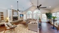Located at 32 Olde Eastwood Village Blvd in Asheville, NC, this thoughtfully designed single-floor space combines classic architectural details with warm, inviting finishes. The open-concept layout encompasses a combined kitchen and living room that makes efficient and elegant use of the available floor area.

The living room is the centerpiece of the space, showcasing soaring vaulted ceilings that lend a sense of grandeur and openness. A dramatic floor-to-ceiling stacked stone fireplace serves as the focal point of the room, flanked by built-in white shelving that adds both function and style. Rich hardwood flooring runs throughout, complementing the neutral tones of the walls and trim. Large arched and rectangular windows line the walls, flooding the interior with natural light and offering views of the surrounding lush greenery.

Two ceiling fans are mounted at varying heights to accommodate the vaulted ceiling, ensuring comfort throughout the space. Recessed and track lighting provide additional illumination alongside the abundant daylight.

The kitchen area features gleaming granite countertops and a clean, modern aesthetic. A secondary seating area with bistro-style high-top tables sits adjacent to a wall of windows overlooking an outdoor pool, creating a bright and versatile dining or lounging spot. Crown molding throughout adds a refined finishing touch to this well-appointed Asheville retreat.